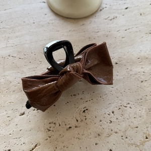 Brown glossy leather bow hair claw clip with vintage design on a beige stone background