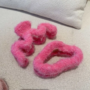 Close-up of bright pink plush hair claw and heart headband on beige woven fabric