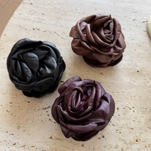 Three 3D rose hair claws in black, burgundy and caramel brown on a stone surface