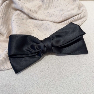 Barrette à grand nœud en satin noir élégante posée sur un pull en maille de couleur crème