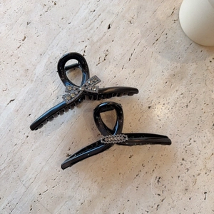 Oversized black hair claw clips with rhinestones and bow design on beige stone surface