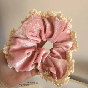 Detail of pink velvet scrunchie with beige lace edges and a gold metal charm