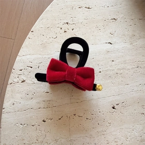 Elegant black hair claw clip featuring a large red velvet bow and a small gold bell accessory