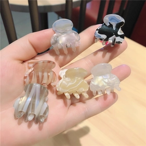 Set of six mini acetate hair claws in assorted marble and amber patterns held in hand