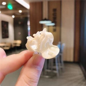 Detailed macro of a cream marble flower hair claw clip held against a warm cafe background