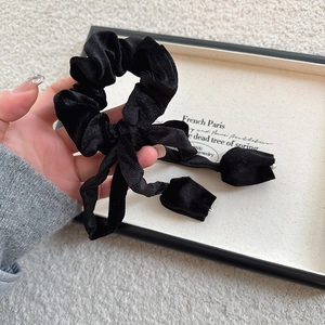 Detail of black velvet scrunchie with long ribbons and pearl accents on a tray