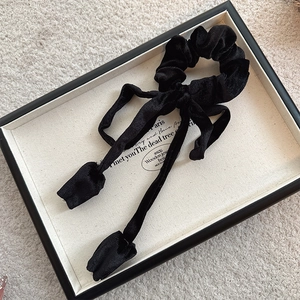 Detail of elegant black velvet hair tie with long ribbon on a white textured background