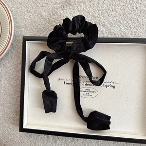 Close-up of black velvet scrunchie with long ribbons on a minimalist display