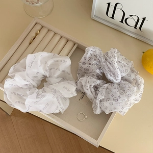 Close-up of white organza scrunchies with Be Nice text and floral monogram print