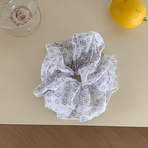 Macro shot of white organza scrunchie with floral monogram patterns on a soft desk
