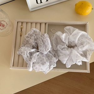 Detailed view of grey patterned and white lettered mesh hair scrunchies on a cream tray