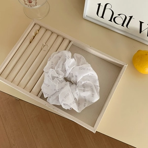 Macro shot of white organza scrunchie with BE NICE print on a beige velvet jewelry tray