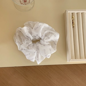Close-up of white mesh scrunchie with grey BE NICE letter print on wooden surface