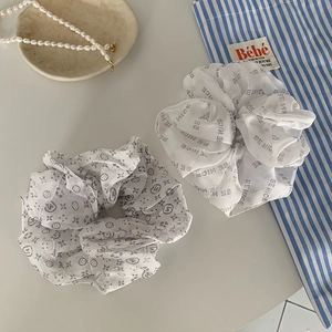 Detail of white mesh scrunchies with letter prints and vintage patterns on white table
