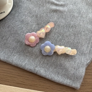 Dettaglio di fermagli per capelli in acrilico con fiori e cuori su tessuto grigio