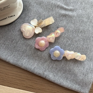 Dettaglio di tre fermagli in acrilico con cuori perlati e strass su sfondo decorativo