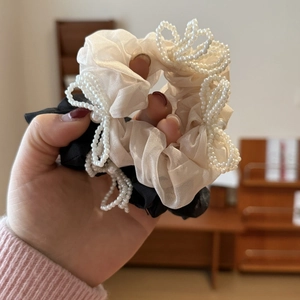 Macro detail of cream tulle and black fabric scrunchies with white pearl bow accents
