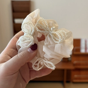 Close-up of beige tulle scrunchie with a delicate white pearl-woven bow detail