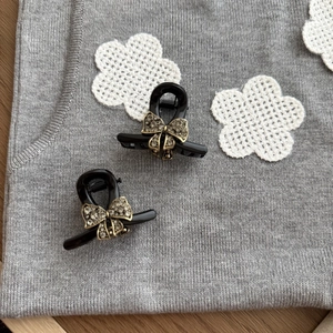 Detail of mini black hair claws with gold-trimmed rhinestone bow on grey knit fabric