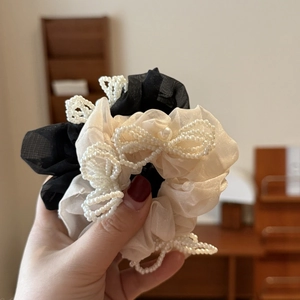 Detail of organza scrunchies in black and beige with pearl bow accents in hand