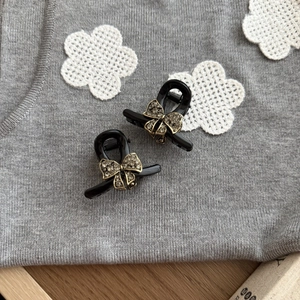 Detail of two mini black bow hair clips with vintage gold rhinestones on a knit fabric