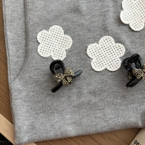 Close-up of two mini black bow hair clips with sparkling rhinestones on grey knit fabric