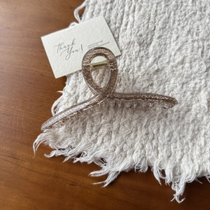 Detailed view of champagne hair claw clip with gold foil texture on a woven white fabric