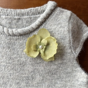 Detail of green silk orchid brooch with white pearl on a grey cable knit sweater