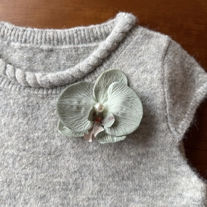 Detail of light green orchid hair clip with realistic petals and a white pearl center