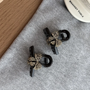 Close-up of two mini black hair claws with sparkling rhinestone golden bow details