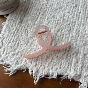 Close-up of a pink macaron resin hair claw clip with golden metal spring on a linen cloth