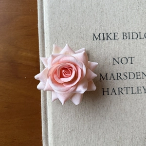 Close-up of light pink faux rose hair clip resting on a vintage beige fabric book cover