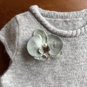 Elegant green orchid hair clip with pearl detail pinned on a grey knit sweater