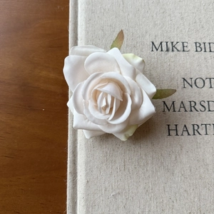 Close-up of a realistic white silk rose head with green leaves on a book's edge