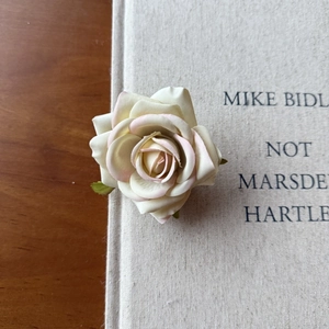 Close-up of artificial velvet rose hair clip with cream petals and pink edges on a book
