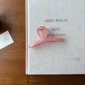 Détail macro d'une grande pince à cheveux rose givrée avec ressort sur livre en lin