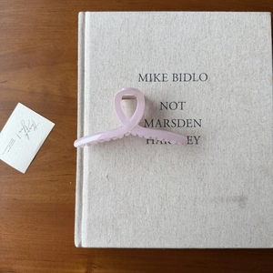 Vue à plat d'une grande pince à cheveux rose clair en acrylique sur un livre de déco