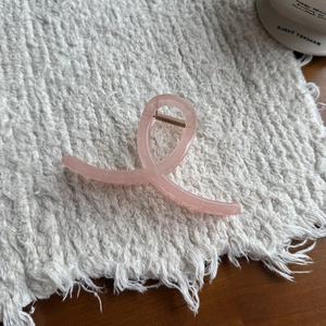 Pink translucent jelly hair claw clip with a minimalist cross design on a white textured mat