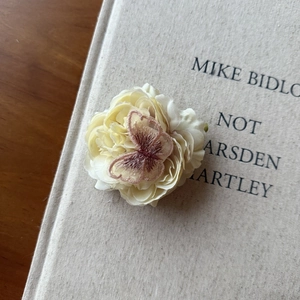 Detail of cream floral hair clip with embroidered brown butterfly on vintage book background