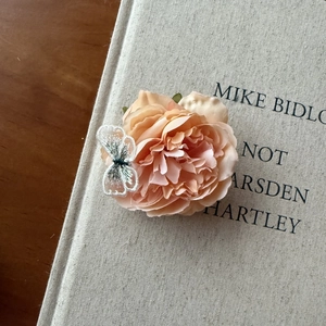Detail of peach fabric flower hair clip with delicate embroidered butterfly accent
