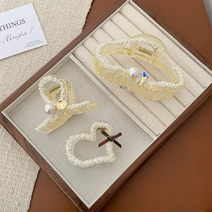Detail of three cream resin hair claws with pearls, rhinestones and brown bows on wood