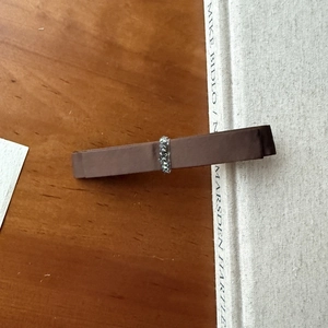 Close-up of brown ribbon bow hair clip with dark grey rhinestone buckle on wood surface