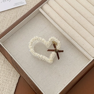 Detail of heart-shaped pearl hair claw clip with brown bow and gold heart pendant