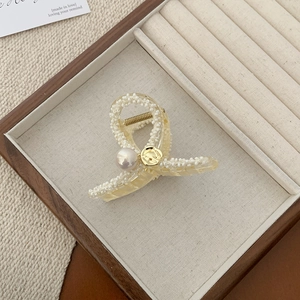 Macro detail of elegant pearl hair claw clip with woven texture and gold metal accents