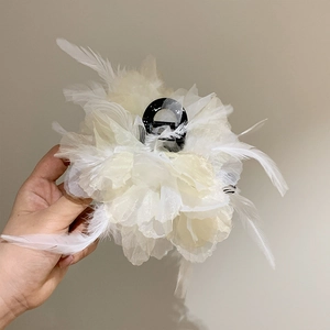 Macro shot of white fabric flower hair claw clip with delicate feathers and translucent petals