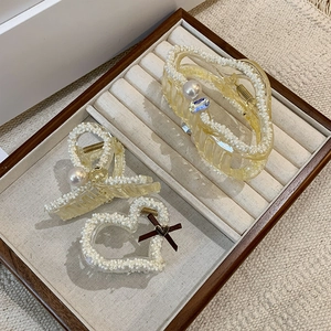 Detailed view of irregular acrylic hair claws with white pearls and brown bow accents