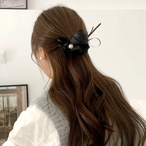 Detailed back view of a satin black rose hair tie with a center pearl worn on long hair