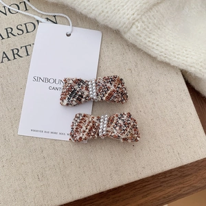 Detail of tweed bow hair clip set with elegant pearls on textured beige canvas background