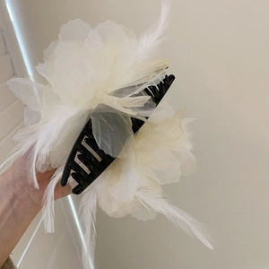 Detail view of a large white bow hair claw with elegant feathers and silk petals