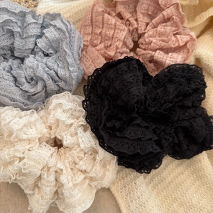 Detail of four lace scrunchies in grey, pink, white, and black with layered pleat texture